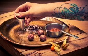 Tavern patisserie, © Niederösterreich Werbung/Andreas Hofer Close-up of a hand with a tattoo decorating chocolate on a plate.