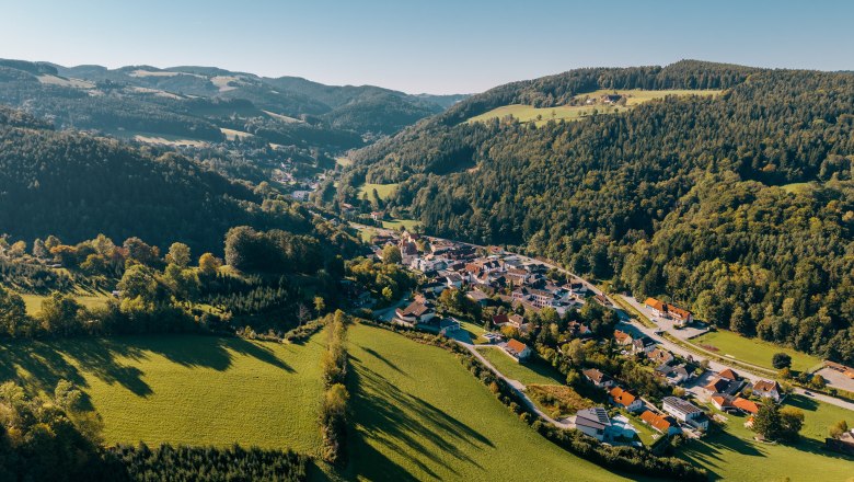 Edlitz town center with fortified church, © Wiener Alpen/Roman Königshofer Photography Aerial view of Edlitz with fortified church, surrounded by green hills and forests.