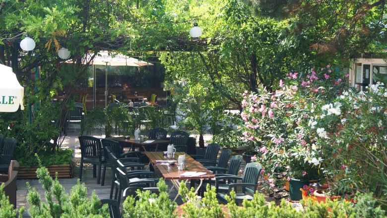 Garden, © sambiente A green garden with tables and chairs, surrounded by trees and flowering shrubs.
