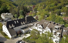 The Hotel Restaurant Höldrichsmühle in a beautiful forest location in Hinterbrühl near Vienna, © Hotel Höldrichsmühle, Jelena Moser Aerial view of a large building complex surrounded by green trees and hills.