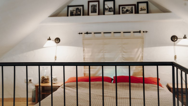 Double bed under the roof, © Weinakademie Retz Attic room with double bed, red pillows and wall lamps.