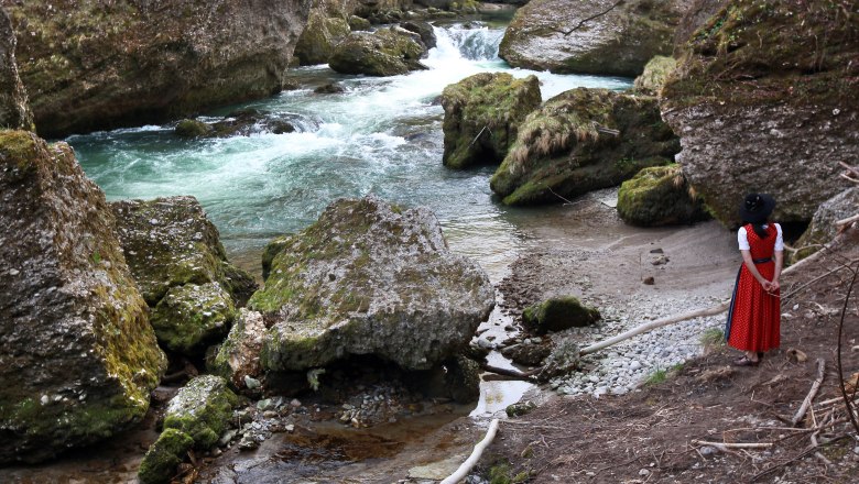 Wonderful - a hike through the gorge, © weinfranz.at A woman in traditional dress stands on the bank of a river in a rocky gorge.