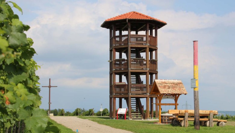 Observation tower on the Sandberg in Roseldorf, © Gemeinde Sitzendorf/ Schmida A wooden observation tower with a red roof stands on a hill next to a cross and a bench. The sky is cloudy.