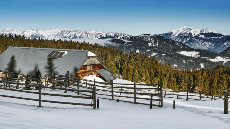 Kranichberger Schwaig, © noew-liebert Snow-covered alpine hut with solar panels, surrounded by forest and mountains.