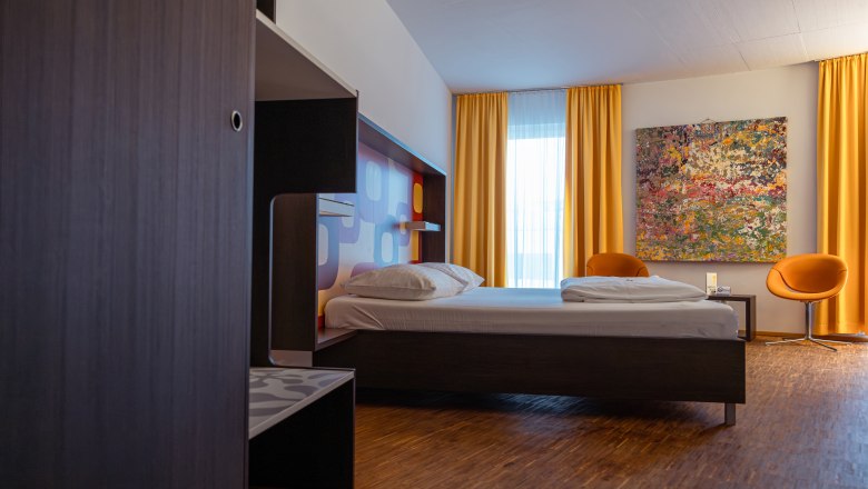 arte Hotel Krems, © Niederösterreich Werbung / Maximilian Pawlikowsky Modern hotel room with bed, yellow curtains and colorful painting on the wall.