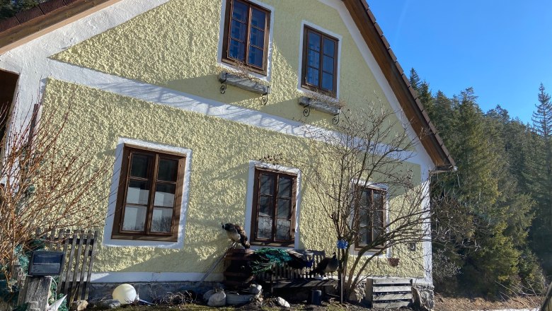 Nazbauerhof, © Wiener Alpen Yellow house with brown windows, surrounded by trees and blue sky.