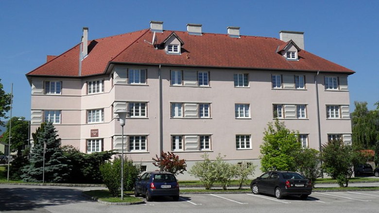 Schuberthof in Wimpassing, © frei Residential building with a red roof and several windows, surrounded by trees and parked cars.