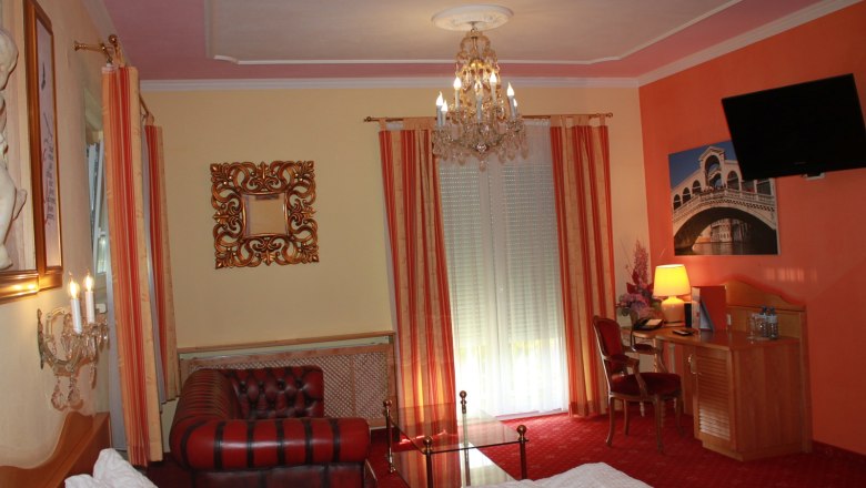 Suite, © Nimal Poudel Elegant hotel room with chandelier, leather sofa, desk and large window with curtains.