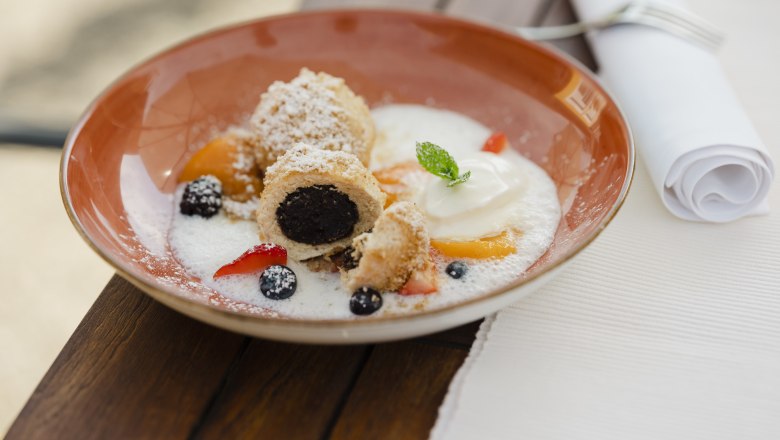 Poppy seed and curd cheese dumplings, © Niederösterreich Werbung/Michael Reidinger A plate of poppy seed and curd cheese dumplings, garnished with fruit and cream, on a wooden table.