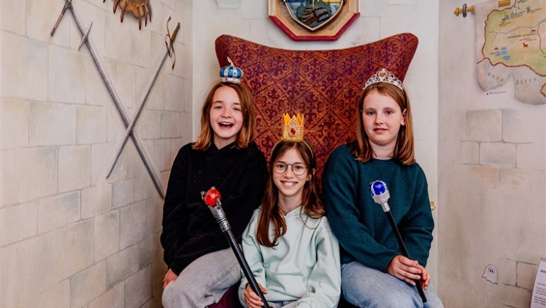Fairytale Hotel Waldpension Nebelstein, © Waldviertel Tourismus, Matthias Streibel Three children with crowns and sceptres sit on a throne in a fairytale room.