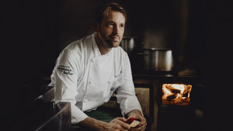 Herbert Bonka's roast pork comes out of the 100-year-old wood-fired oven, © Niederösterreich Werbung/Sophie Menegaldo Cook in white uniform in front of a traditional stove with fire.