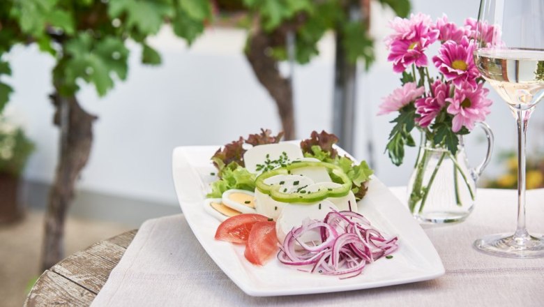 Heurigen delicacies with Johanna Fink, © Philipp Monihart A plate of cheese, onions, tomatoes and salad on a table with flowers and a glass of white wine.