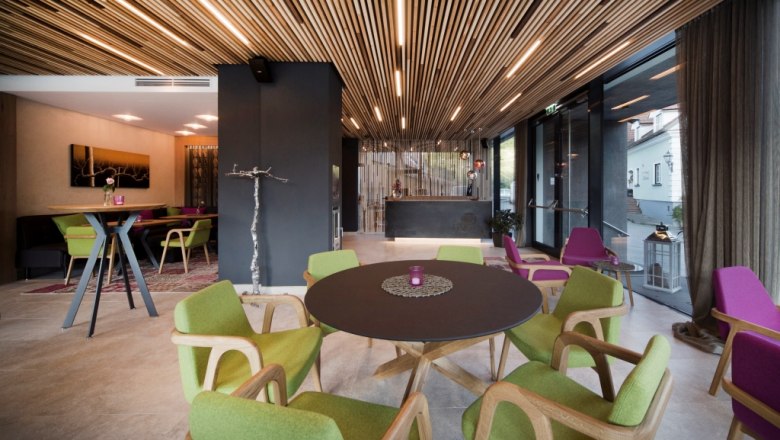 Boutique hotel "Das WeinSpitz", © © photography_pfeffel_at Interior view of a modern hotel lounge with wooden elements, green and purple chairs and a round table.
