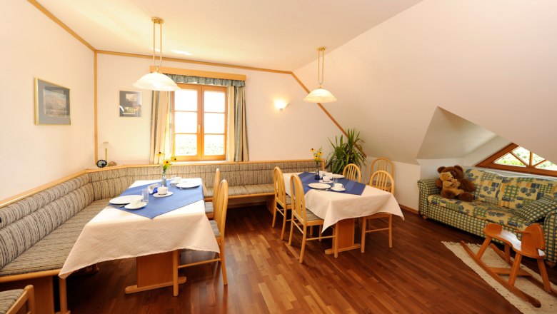 Breakfast area, © Gästehaus Krappel Cozy breakfast area with wooden furniture, laid tables and a sofa with teddy bears.