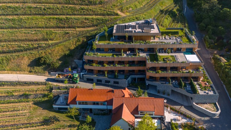 Wine Hotel Nigl, © Niederösterreich Werbung / Maximilian Pawlikowsky Aerial view of a modern hotel with terraces and green roofs, surrounded by vineyards.