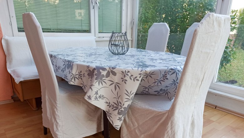Dining area, © Multimedia Lauda Dining area with table, chairs and bench, tablecloth with floral pattern, window in the background.