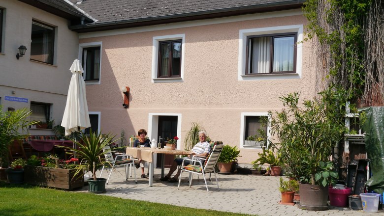 Terrace in the inner courtyard, © fbeck Two people are sitting at a table on a terrace in the courtyard of a house with plants and a parasol.