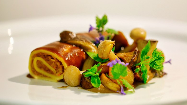 Delicacies from the award-winning kitchen, © Familie Görg Gourmet dish with mushrooms and fresh herbs served on a white plate.
