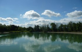 Lake Ebersdorf, © zVg Gemeinde Ober-Grafendorf A calm lake with trees and clouds reflected in the water.