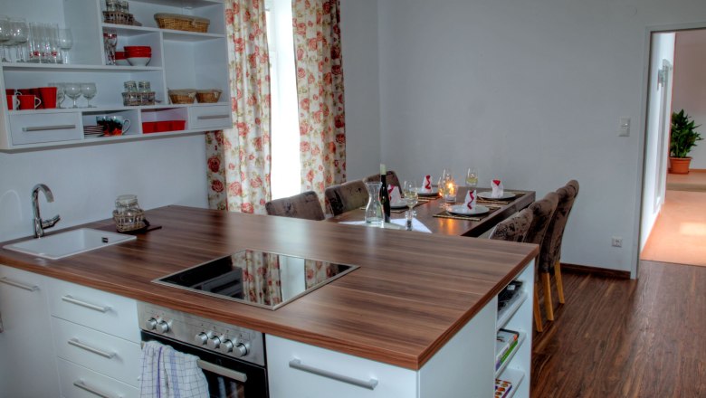 View of the dining table in Loft 1, © Carlos de Mello Modern kitchen with dining table in a loft, decorated with floral pattern curtains.