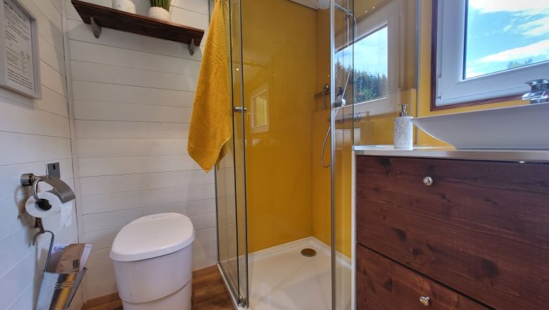 Bathroom, © Villa to go Modern bathroom with yellow shower screen, white WC, wooden shelf and window.