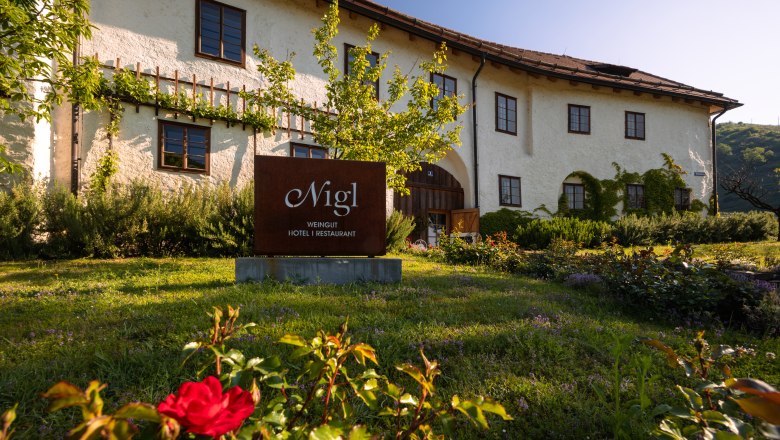Wine Hotel Nigl, © Niederösterreich Werbung / Maximilian Pawlikowsky Exterior view of the Weinhotel Nigl with garden and sign.