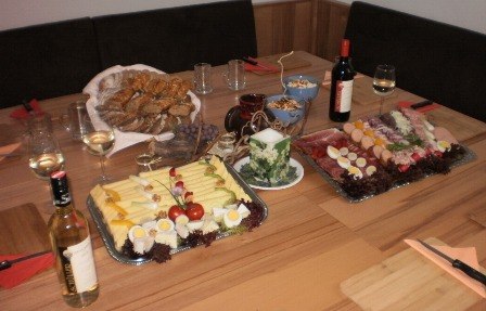 Delicacies at the winery, © Familie Schüller A laid table with cheese and sausage platters, bread, wine and glasses.