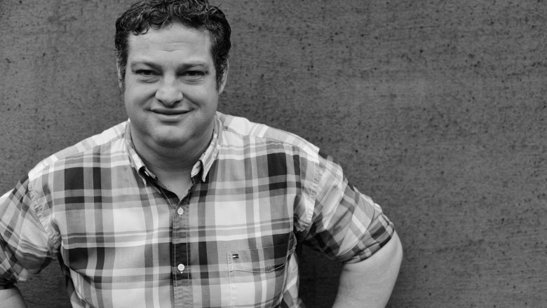 Christian Edelmann, Winery Edelmann Göttlesbrunn, © Die Rubin Carnuntum Weingüter Black and white photo of a man in a plaid shirt in front of a concrete wall.