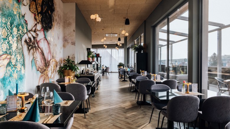 Roof Top Bar, © Bernhard Raab Interior view of a stylish restaurant with large windows and artistic murals.