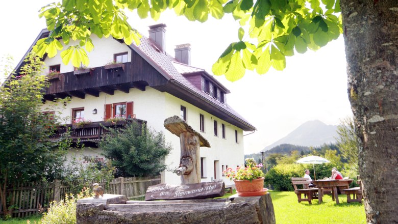 Steinwandhof, © weinfranz.at A traditional farmhouse with a wooden balcony, surrounded by green nature and a tree in the foreground.