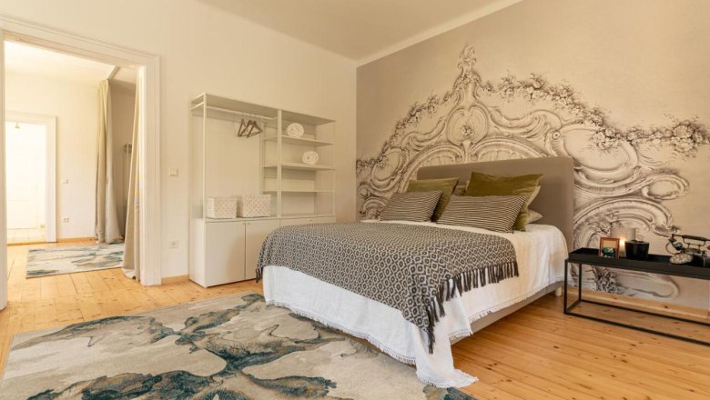 Example sleeping area, © Guestia GmbH A stylishly furnished bedroom with a large bed, decorative cushions, a rug and an artistic wall design.