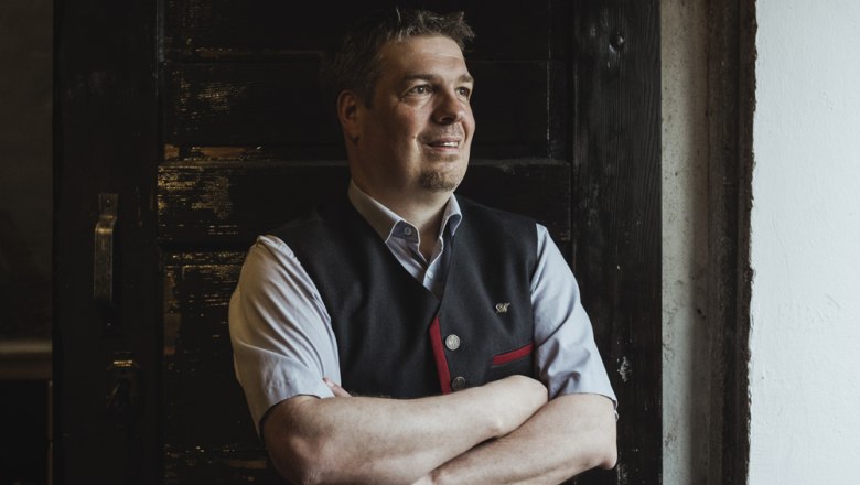 Landlord Dietmar Schöner, © Niederösterreich Werbung/David Schreiber A man in traditional dress stands with his arms folded in front of a dark wooden door.
