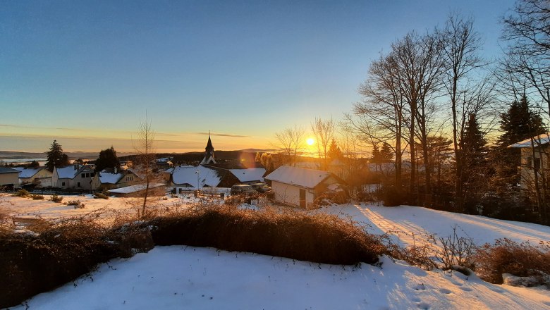 Sunrise view in winter, © Christoph Gierlinger Winter landscape with sunrise over a snow-covered village and bare trees.