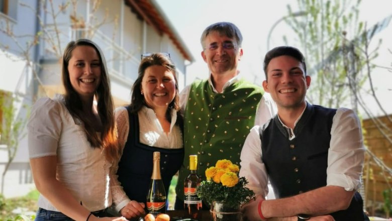 The Wiesinger family, © Weinbau Wiesinger Four people in traditional dress stand around a wine barrel with flowers and bottles.