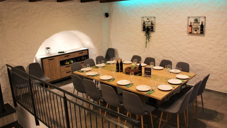 Wine shop, © Weingut Kerner A stylishly laid table in a wine cellar with modern gray chairs and decorative lighting.