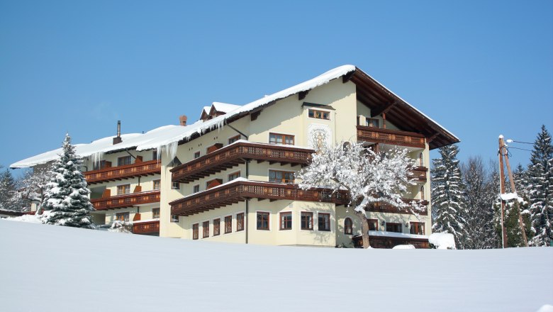Ramswirt in winter, © Ramswirt, Familie Pichler A large, traditional building in the snow with wooden decorations and a snow-covered tree in the foreground.