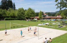 Aspang outdoor pool, © Freibad Aspang Children play volleyball on a sand court at the Aspang outdoor pool, surrounded by green meadows and trees.