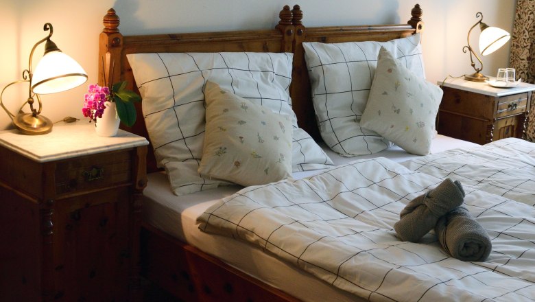 Double room, © Reinhard Maurer Cozy double room with wooden furniture, bed with checkered bedding, bedside tables and lamps.