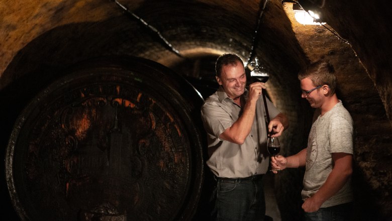 Palatinate winegrowing family, © Astrid Bartl Two men in a wine cellar, one is holding a wine tasting from a barrel.