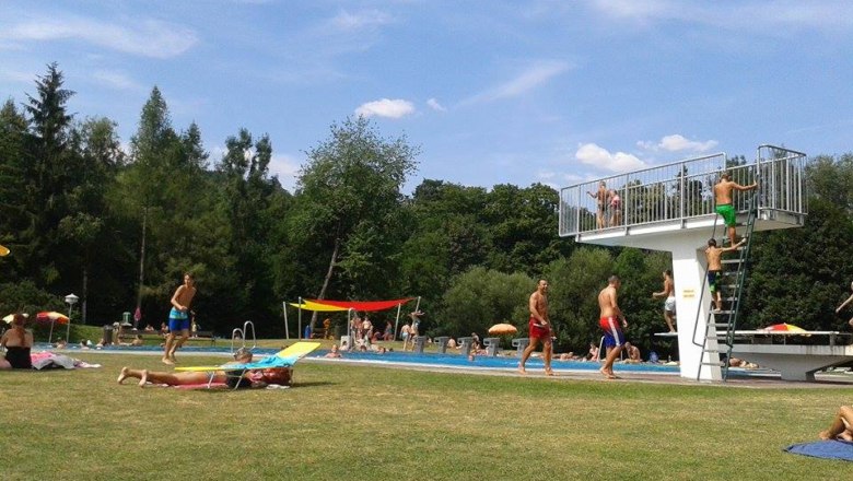 Parkbad Seebenstein, © Ines Hattenhofer People in the Seebenstein park pool, some on the lawn, others in the pool. A diving tower can be seen.