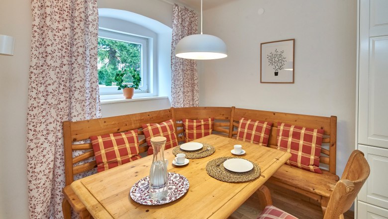 Top 3 - Dining area, © VP FeWo OG Cozy dining area with wooden table, corner bench and checkered cushions.
