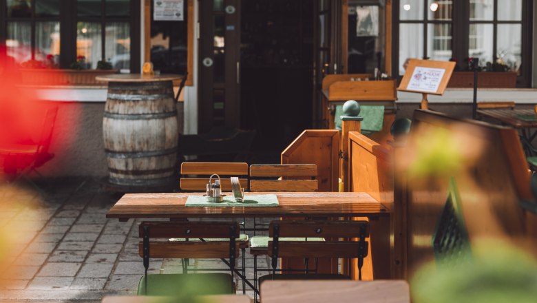 Town pub with guest garden, © Niederösterreich Werbung/David Schreiber An empty table with wooden chairs in a guest garden, in the background a wine barrel and an entrance.