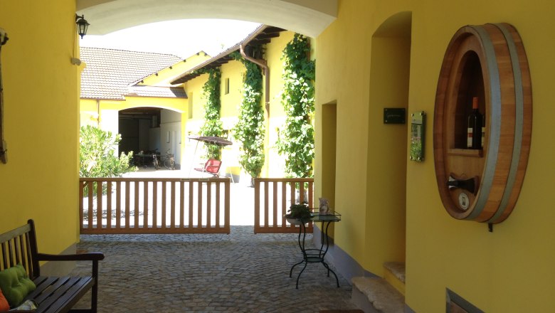 Winzerhof & Guesthouse Greil, © M. Greil Inner courtyard of a yellow building with wine barrel decoration and wooden gate.