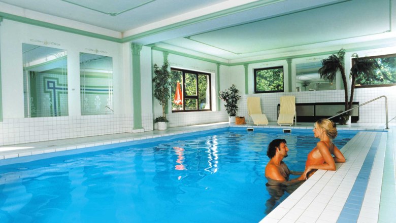 Pool, © Das Steinberger A couple in the pool of an elegant indoor area with plants and sun loungers.