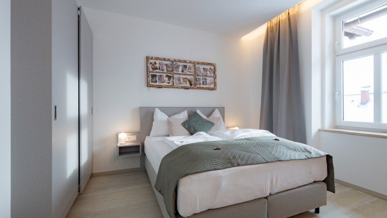 Apartment 3, © Atelier Fürtner-Ton Modern bedroom with double bed, gray curtains and wall decoration.