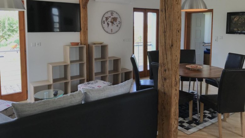 Living area, © Familie Mokesch Modern living area with wooden beams, dining table, chairs, wall shelf, clock and TV.