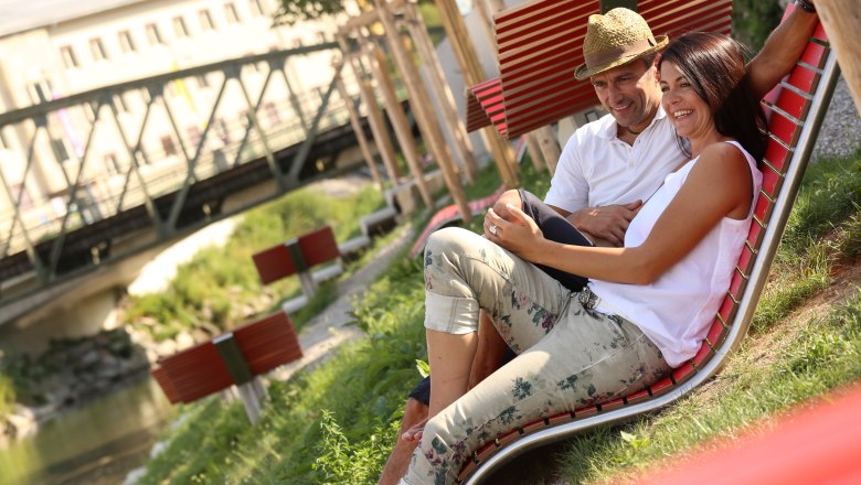 Erlaufhafen meeting zone, © schwarz-koenig.at A couple sits relaxing on a red lounger outside, near a bridge.