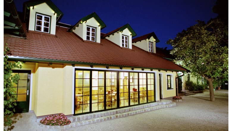 Schaflerhof, © Weingut Schaflerhof A building with a yellow façade and red roof tiles at night, illuminated from the inside.