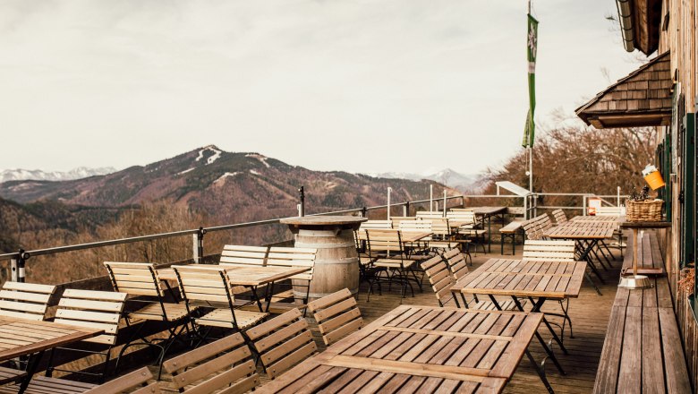 From the terrace, © Stefanie Rysavi Empty terrace with wooden tables and chairs, mountain landscape in the background.