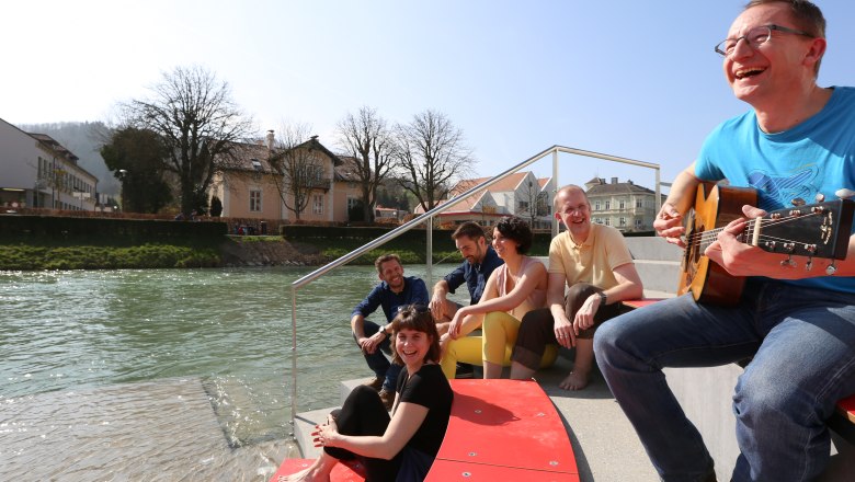 Erlaufhafen pier, © schwarz-koenig.at Group of people sitting on a riverbank laughing, one person playing the guitar.